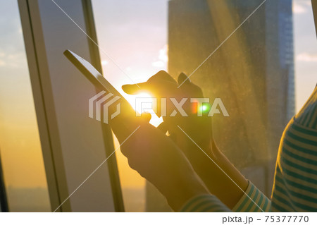 Woman using smartphone against sunset cityscape view through window - close up Woman using smartphone against sunset cityscape view through window - close up 75377770