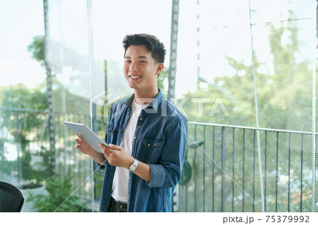 Portrait of a young confident smiling indian man holding a tablet and looking into the distance 75379992