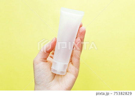 Female hand holding cream tube cosmetic products on yellow background 75382829