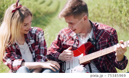 Man and woman in a field on spring day. Couple in love spend time in spring field. Grass on background. Man with electro guitar. 75385969