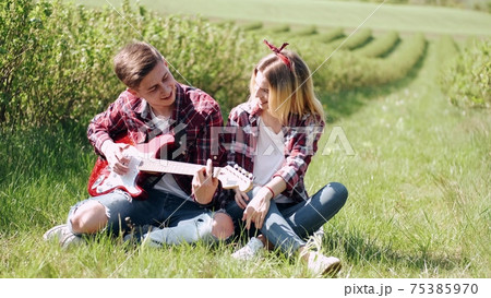 Man and woman in a field on spring day. Couple in love spend time in spring field. Grass on background. Man with electro guitar. Man and woman in a field on spring day. Couple in love spend time in spring field. Grass on background. Man with electro guitar. 75385970