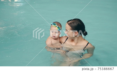 Mom teaches infant son to swim in the pool at water park Mom teaches infant son to swim in the pool at water park 75386667