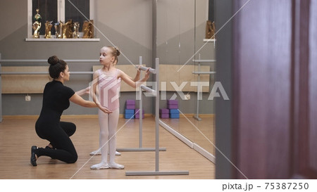 Ballet teacher professional ballerina helping girl train near the barre Ballet teacher professional ballerina helping girl train near the barre 75387250