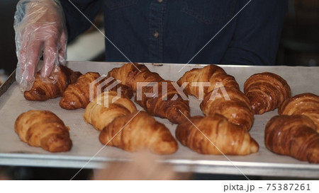 Woman in gloves checks freshly baked croissants on a tray Woman in gloves checks freshly baked croissants on a tray 75387261