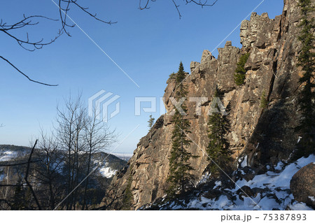 An extended brown rock wall with a mound of large boulders at the foot 75387893