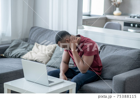 A dark-skinned young man working on a laptop and feeling tired 75388115