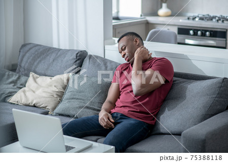 A dark-skinned young man working on a laptop and feeling tired 75388118