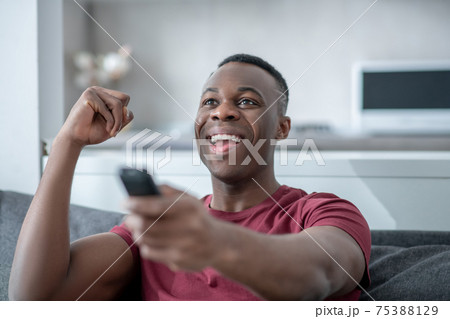 A dark-skinned young man watching tv and looking excited A dark-skinned young man watching tv and looking excited 75388129