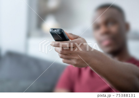 A dark-skinned young man spending time at home and switching on tv A dark-skinned young man spending time at home and switching on tv 75388131