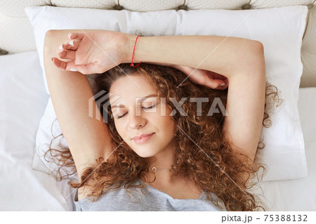 Horizontal portrait of sleepy cute female with curly hair, pleasant appearance, feels relaxed and sees good dreams, lies in comfortable bed, enjoys calm domestic atmopshere. Sleeping concept Horizontal portrait of sleepy cute female with curly hair, pleasant appearance, feels relaxed and sees good dreams, lies in comfortable bed, enjoys calm domestic atmopshere. Sleeping concept 75388132