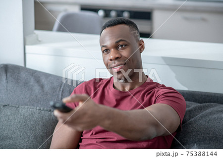 A dark-skinned young man spending time at home and switching on tv A dark-skinned young man spending time at home and switching on tv 75388144