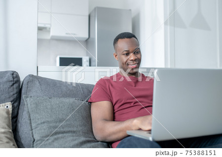 A dark-skinned young man working from home and looking involved A dark-skinned young man working from home and looking involved 75388151
