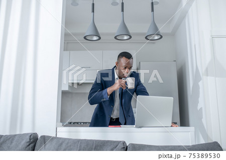Elegant dark-skinned man reading something on laptop and looking excited Elegant dark-skinned man reading something on laptop and looking excited 75389530