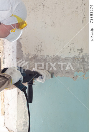 Worker removes old paint from a concrete wall 75393274