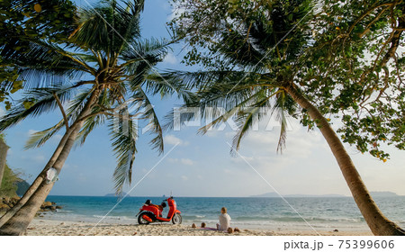 Scooter road trip. Woman alone on red motorbike in white clothes on sand beach by ocean. One girl caucasian tourist walk near tropical palm tree. 75399606