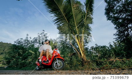 Scooter road trip. Love couple on red motorbike in white clothes on forest road trail. Just married woman and man kiss, hugs, sit on motorbike. Scooter road trip. Love couple on red motorbike in white clothes on forest road trail. Just married woman and man kiss, hugs, sit on motorbike. 75399679