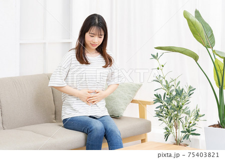 部屋のソファーに座ってお腹に手を当てる若い女性 部屋のソファーに座ってお腹に手を当てる若い女性 75403821
