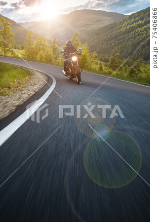 Moto racer riding on forest road during sunset Moto racer riding on forest road during sunset 75406866