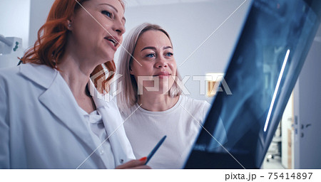 Mature doctor showing promising X ray results to patient Mature doctor showing promising X ray results to patient 75414897