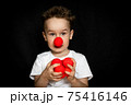 Boy with a clown red nose and red noses in hands. Red Nose Day. 75416146