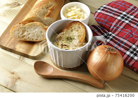 オニオングラタンスープのまわりにフランスパン、チーズ、スプーン、玉葱、ミトン 75416200