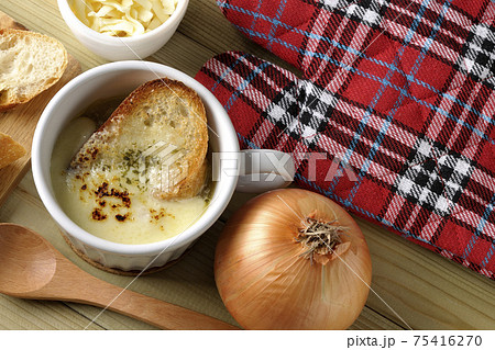 オニオングラタンスープのまわりにフランスパン、チーズ、スプーン、玉葱、ミトン（俯瞰） 75416270