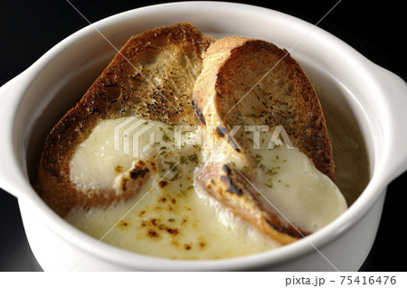 焦げ目のついたチーズ、フランスパンが入ってるオニオンスープを黒背景で撮影 75416476