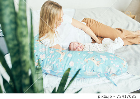 Young mother with baby in bed with a pillow for pregnant women. 75417035