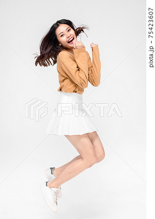 happiness, freedom, motion and people concept - smiling young woman jumping in air over gray background 75423607