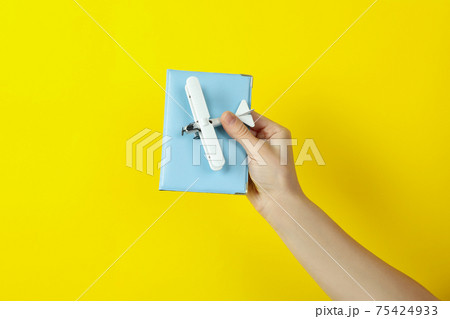 Female hand hold toy plane and passport on yellow background 75424933