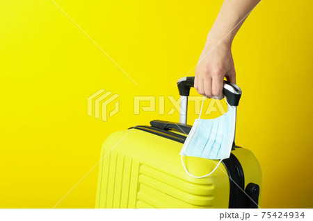Female hand hold travel bag and medical mask on yellow background 75424934