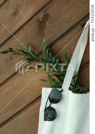 Eco bag with twig and sunglasses on wooden background Eco bag with twig and sunglasses on wooden background 75425036