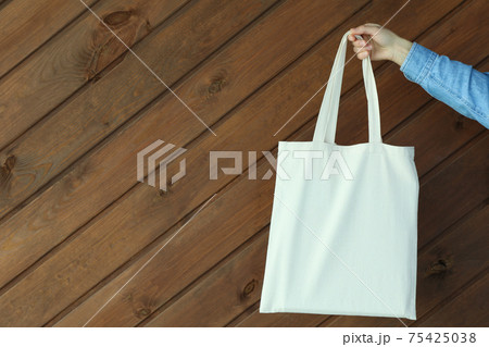Female hand hold eco bag on wooden background Female hand hold eco bag on wooden background 75425038