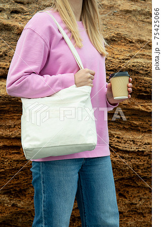 Young woman hold stylish eco bag and paper cup outdoor against big sea stone Young woman hold stylish eco bag and paper cup outdoor against big sea stone 75425066