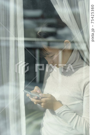 窓辺でスマートフォンを見る女の子(外出自粛要請のイメージ) 窓辺でスマートフォンを見る女の子(外出自粛要請のイメージ) 75425360