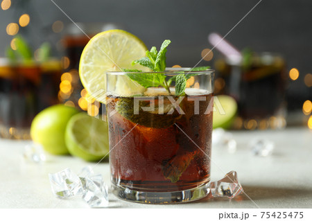 Glass of Cuba Libre on white textured table against blurred lights Glass of Cuba Libre on white textured table against blurred lights 75425475
