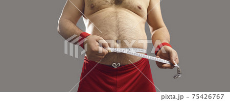 Midsection shot of an overweight man measuring his chubby waist with a tape measure Midsection shot of an overweight man measuring his chubby waist with a tape measure 75426767