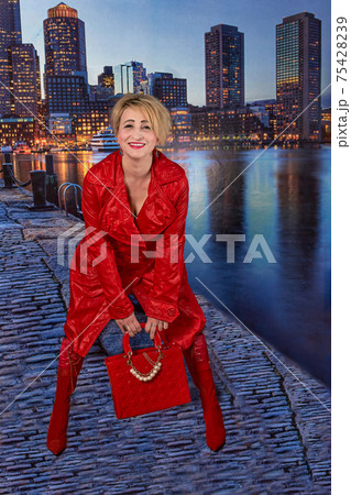 woman in red raincoat boots and a bag posing on the embankment of the night city 75428239