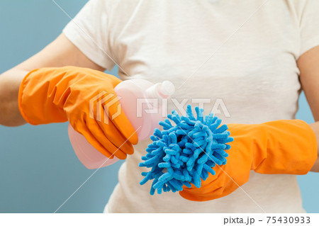 Woman holding a bottle of washing liquid and a rag on a blue background. Woman holding a bottle of washing liquid and a rag on a blue background. 75430933