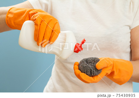 Woman holding a bottle of dishwashing liquid and a sponge on a blue background. 75430935
