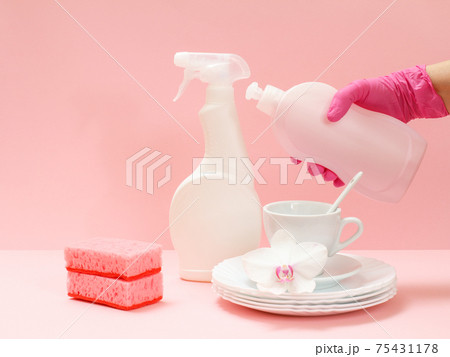 Woman's hand in protective glove with bottle of dishwashing liquid on a pink background. Woman's hand in protective glove with bottle of dishwashing liquid on a pink background. 75431178