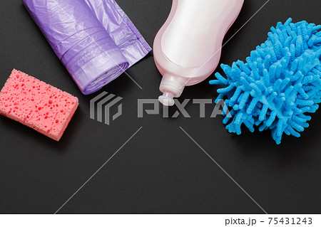 Bottle of washing liquid, garbage bags and a sponge on a black background. 75431243