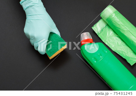 Bottle of washing liquid and a hand with a sponge on a black background. 75431245