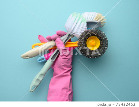 female hand in a pink glove holds a stack of plastic cleaning brushes 75432452