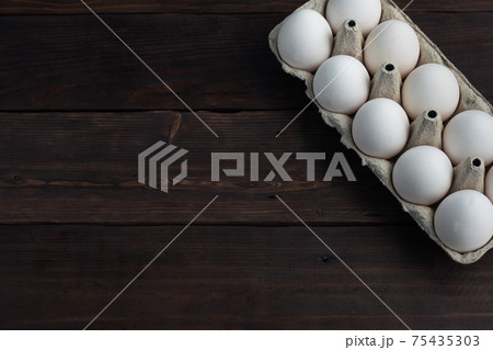 Fresh chicken eggs in a package, raw eggs in a white shell in a box. Top view copy space, wooden background. 75435303
