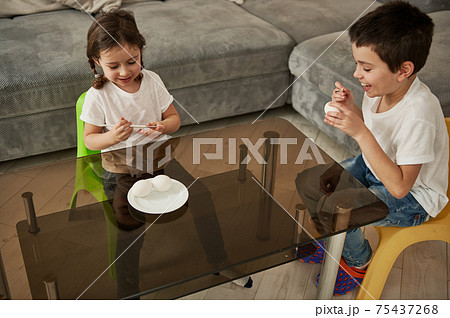 Two adorable children holding eggs and paintbrushes ready for coloring Easter eggs. Easter concept Two adorable children holding eggs and paintbrushes ready for coloring Easter eggs. Easter concept 75437268