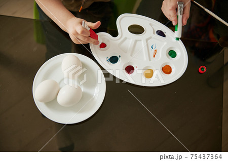 Close-up of a boy's hand squeezing green paint from a tube onto a palette for coloring Easter eggs Close-up of a boy's hand squeezing green paint from a tube onto a palette for coloring Easter eggs 75437364