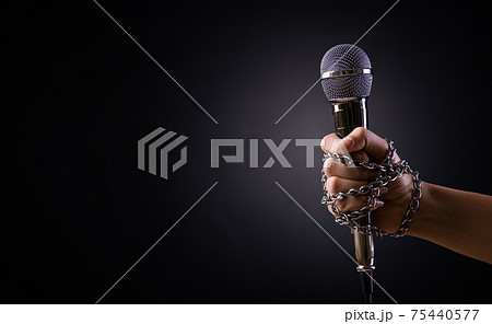 World press freedom day concept. Hand holding a microphone with chain on dark background, symbol of press freedom of speech freedom. World press freedom day concept. Hand holding a microphone with chain on dark background, symbol of press freedom of speech freedom. 75440577