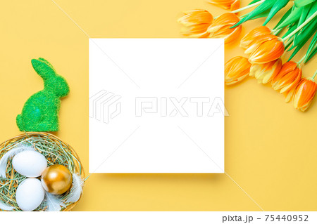Easter luxury. Golden, white colour egg in basket with spring tulips, feathers on pastel yellow background in Happy Easter decoration. Flat lay, top view. 75440952