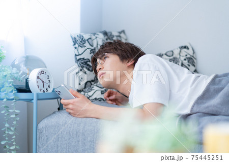 早朝　寝起きにスマホをチェックする若い男性 75445251
